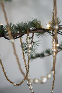 Decorative beaded chains hanging from a branch with blurred lights in the background