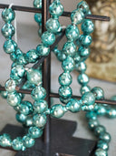 Turquoise green glass Christmas bauble garland draped over a dark metal display stand.