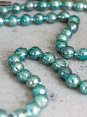 A close-up of metallic teal beads arranged in loops on a light textured surface.
