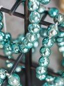 Close-up of strands of reflective teal glass beads draped over a dark metal display stand.
