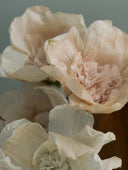 Handmade and hand-dyed crepe paper flowers in solid colors. Bouquets of paper flower Christmas ornaments in blue, white, and pale pink
