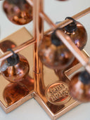 Close-up of a decorative copper-toned metal stand with multiple hanging glass globes and a circular logo plate reading 'deco living' on a white surface.