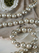 A close-up of metallic silver glass bead garland draped over a beige fabric surface with a white flower prop.
