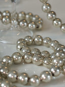 Silver metallic beaded strands arranged on a light surface, with a blurred glass base in the background.
