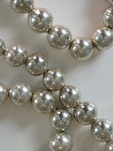 A close-up of metallic silver faceted glass beads draped across a light neutral background.